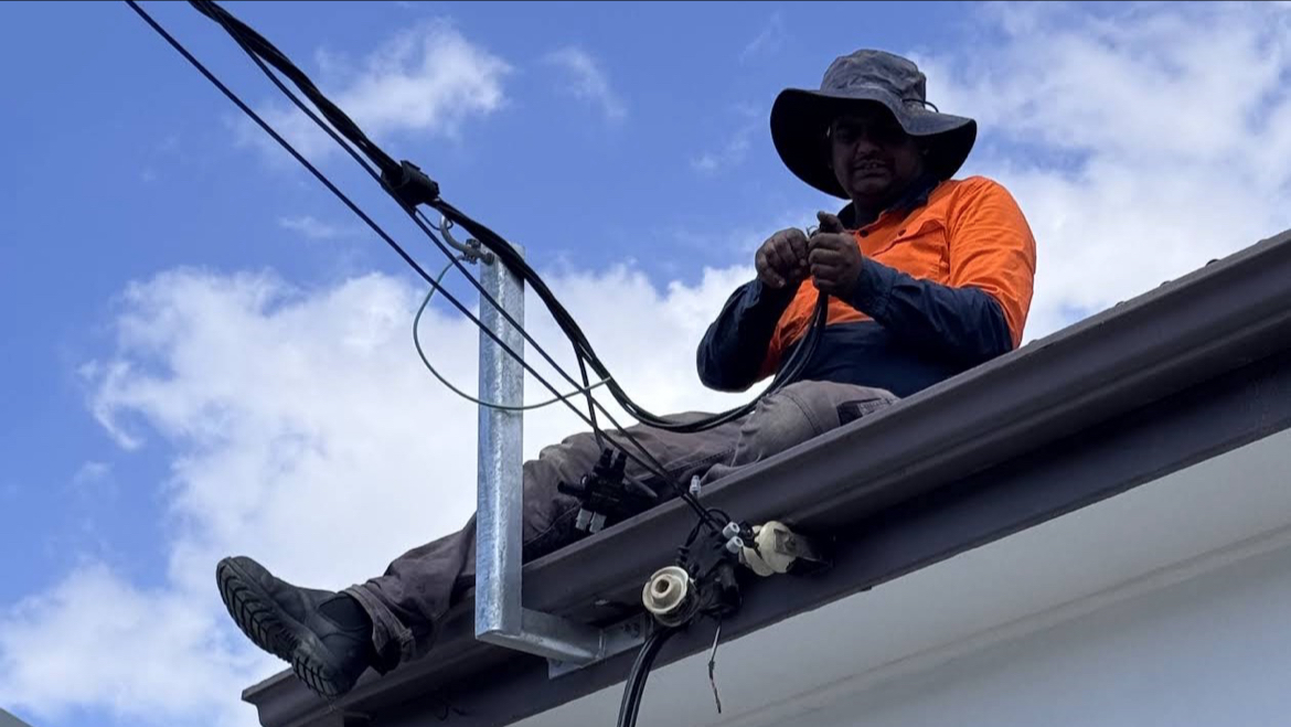 R & M Electricals electrician in hi-vis working on the overhead service cable at a house roofline
