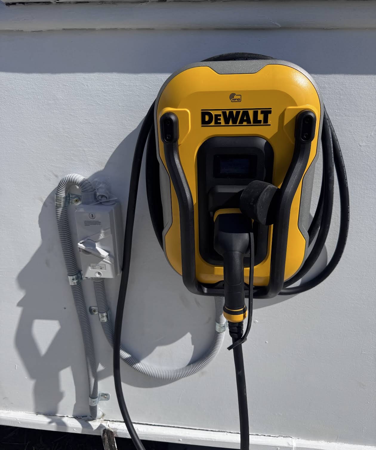 DeWalt EV charger installed on an exterior wall with an isolator switch and conduit