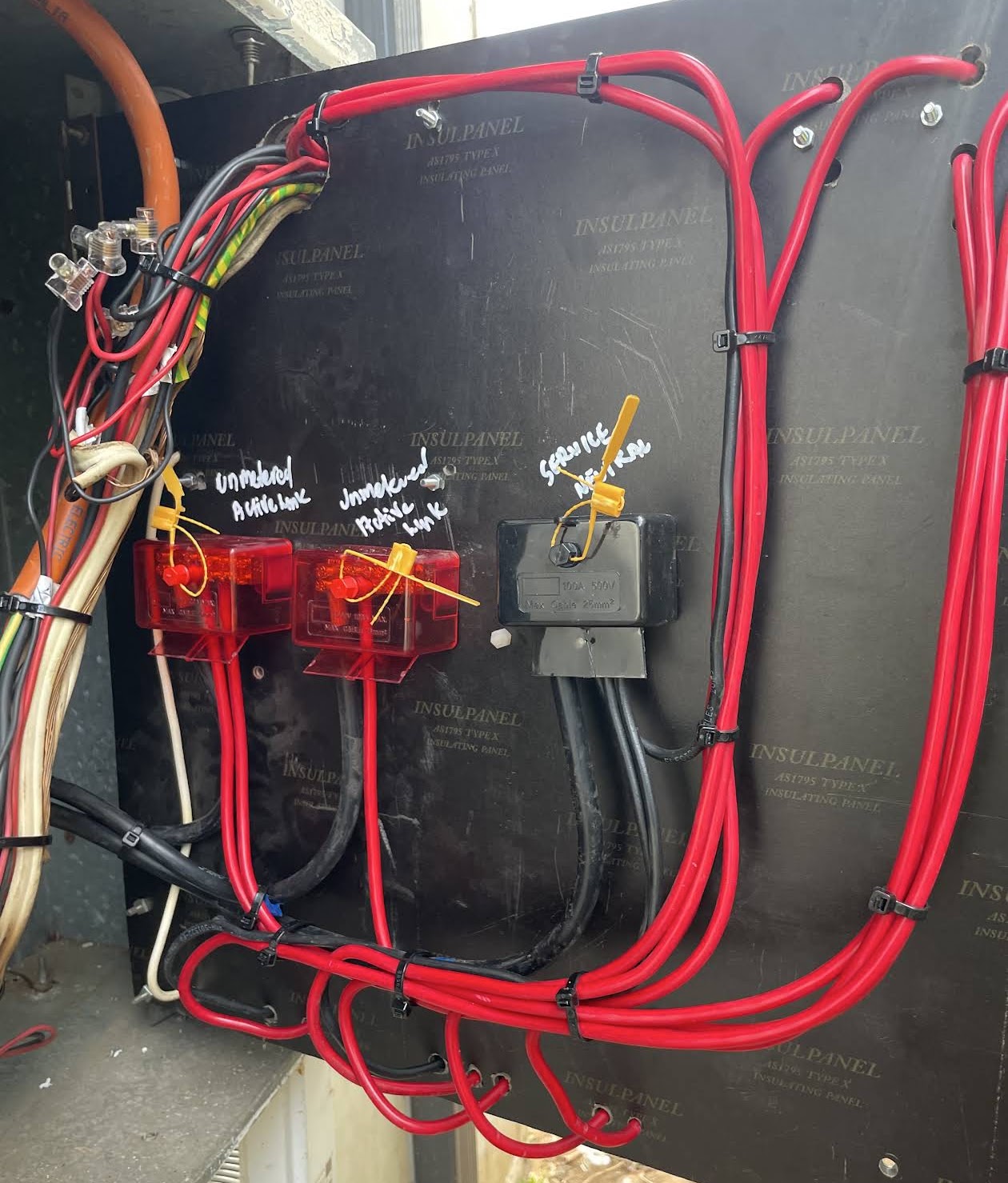 Inside a switchboard with red cabling and hand-labelled service neutral and unmetered links