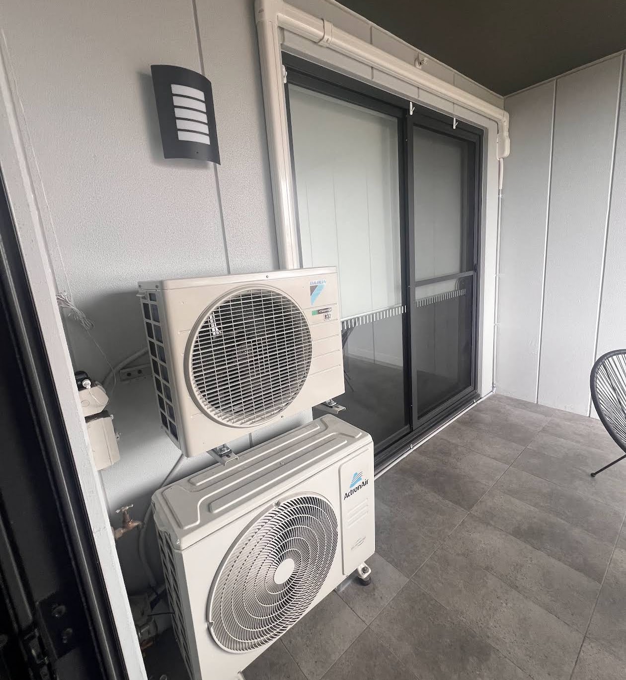 Two split-system air conditioning outdoor units stacked on an apartment balcony